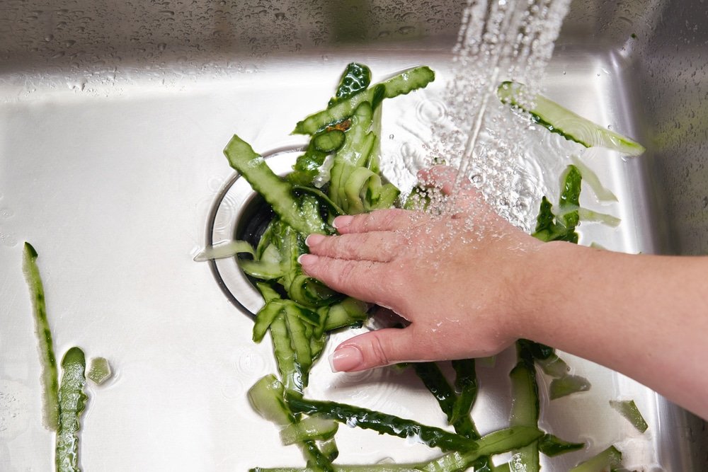hand pushing scraps down a sink garbage shredder