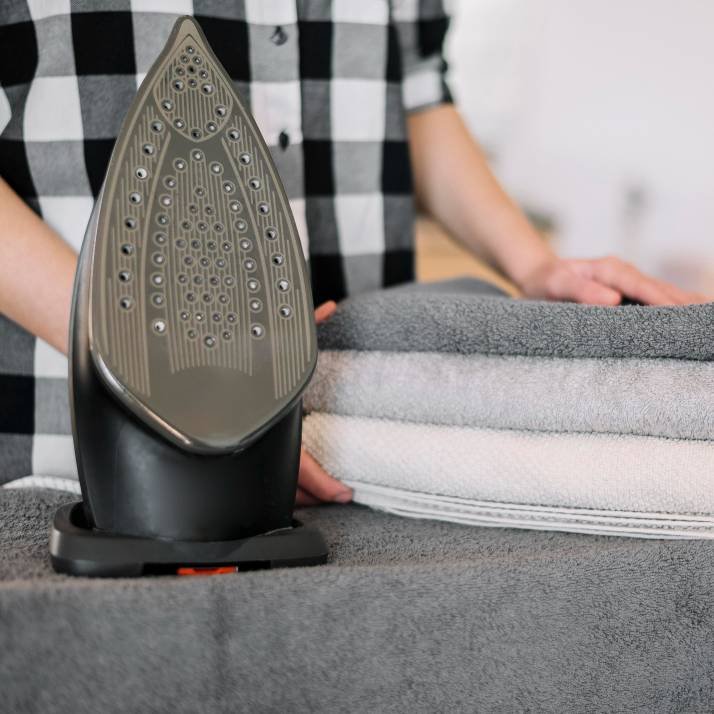 a woman folding towels and a black garment steamer on the ironing board