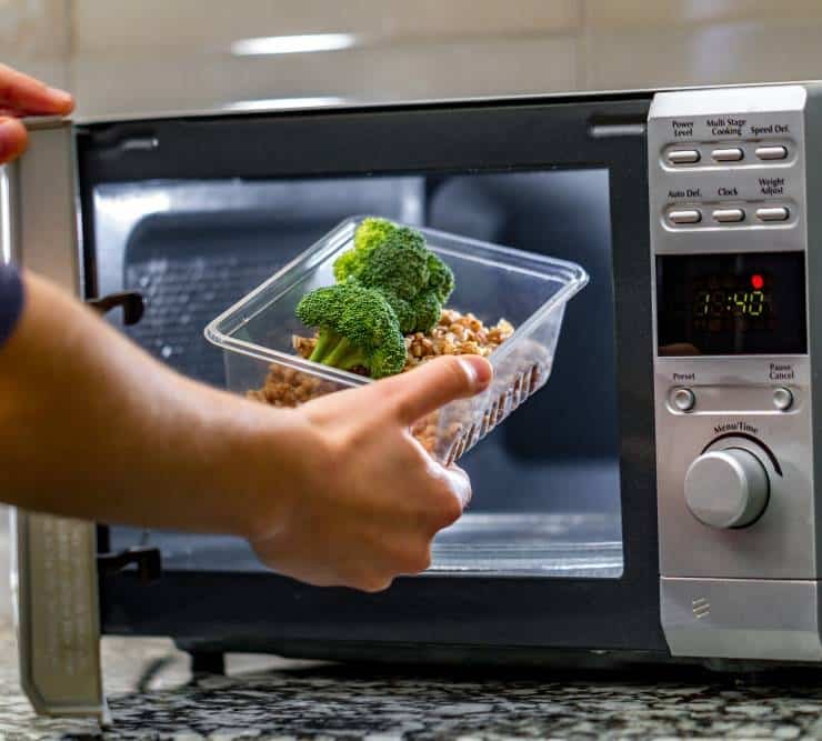 a woman putting a plastic container with broccoli and buckwheat