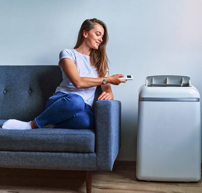 a woman sitting on a sofa next to a portable air conditioner