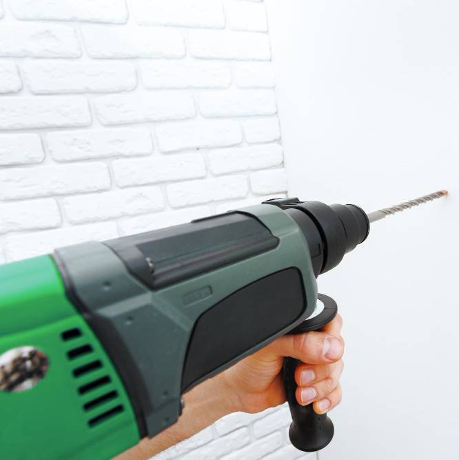 using a hammer drill to drill the wall